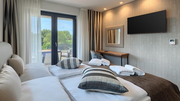 A modern hotel room with a large bed, a flat-screen TV, and a view of the outdoors.