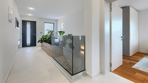A modern hallway with a glass railing, a wooden floor, and a plant.