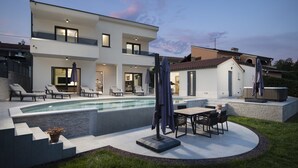 A modern two-story house with a swimming pool, outdoor seating, and a patio area.