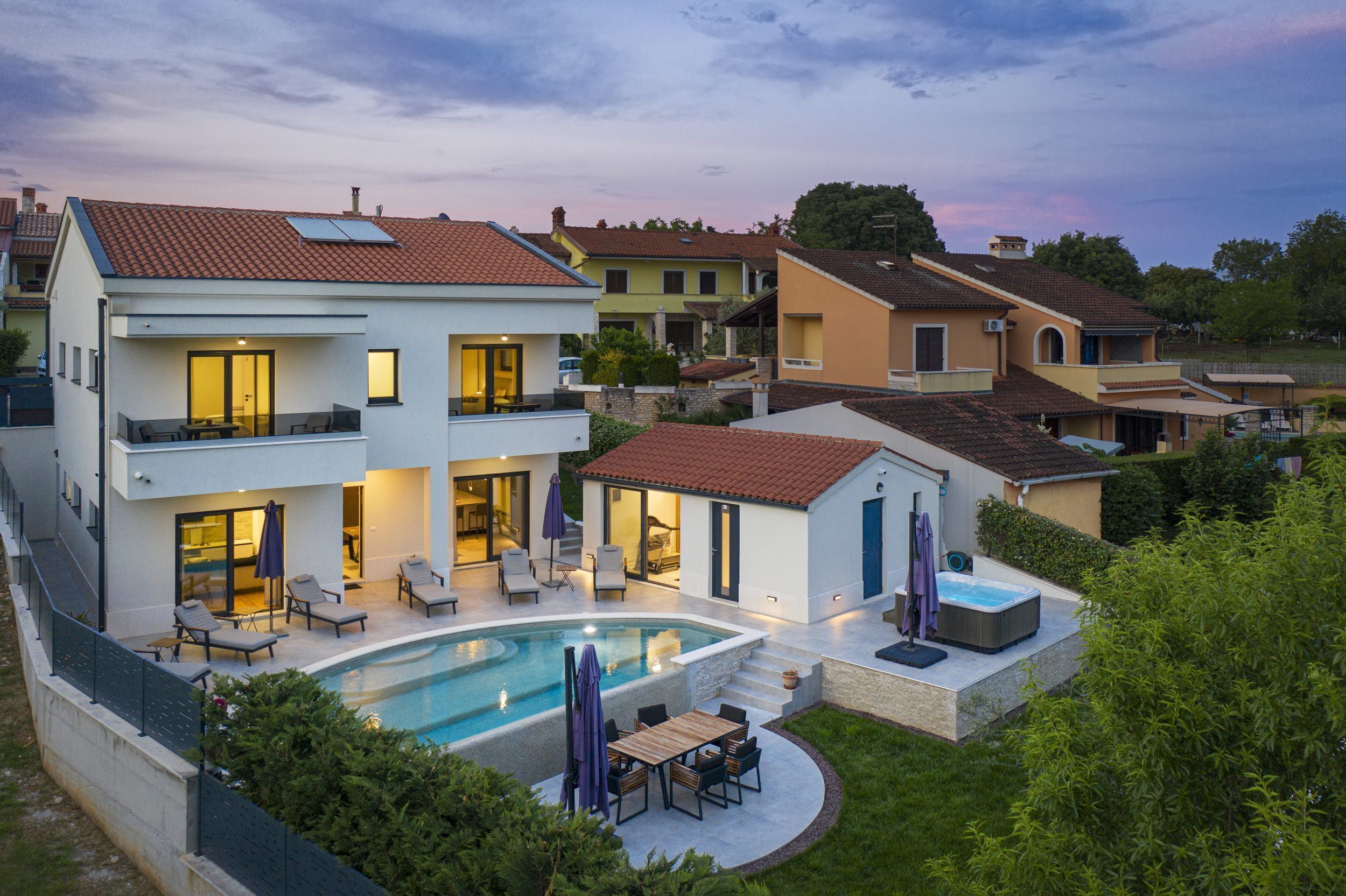 A modern two-story house with a swimming pool, outdoor seating, and a hot tub.