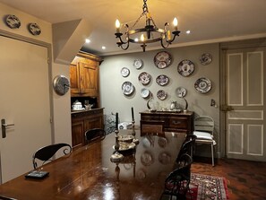 Un coin repas comprenant une table en bois, des chaises, un lustre et des assiettes décoratives accrochées au mur.