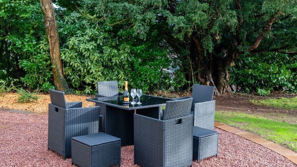 Un área de comedor al aire libre con una mesa y sillas, rodeada de abundante vegetación.