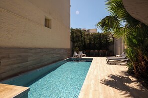 A swimming pool with lounge chairs, a wooden deck, and a building with a textured wall. - The Mansion - Kalamata Mediterranean Suites & Villas (Kalamata)
