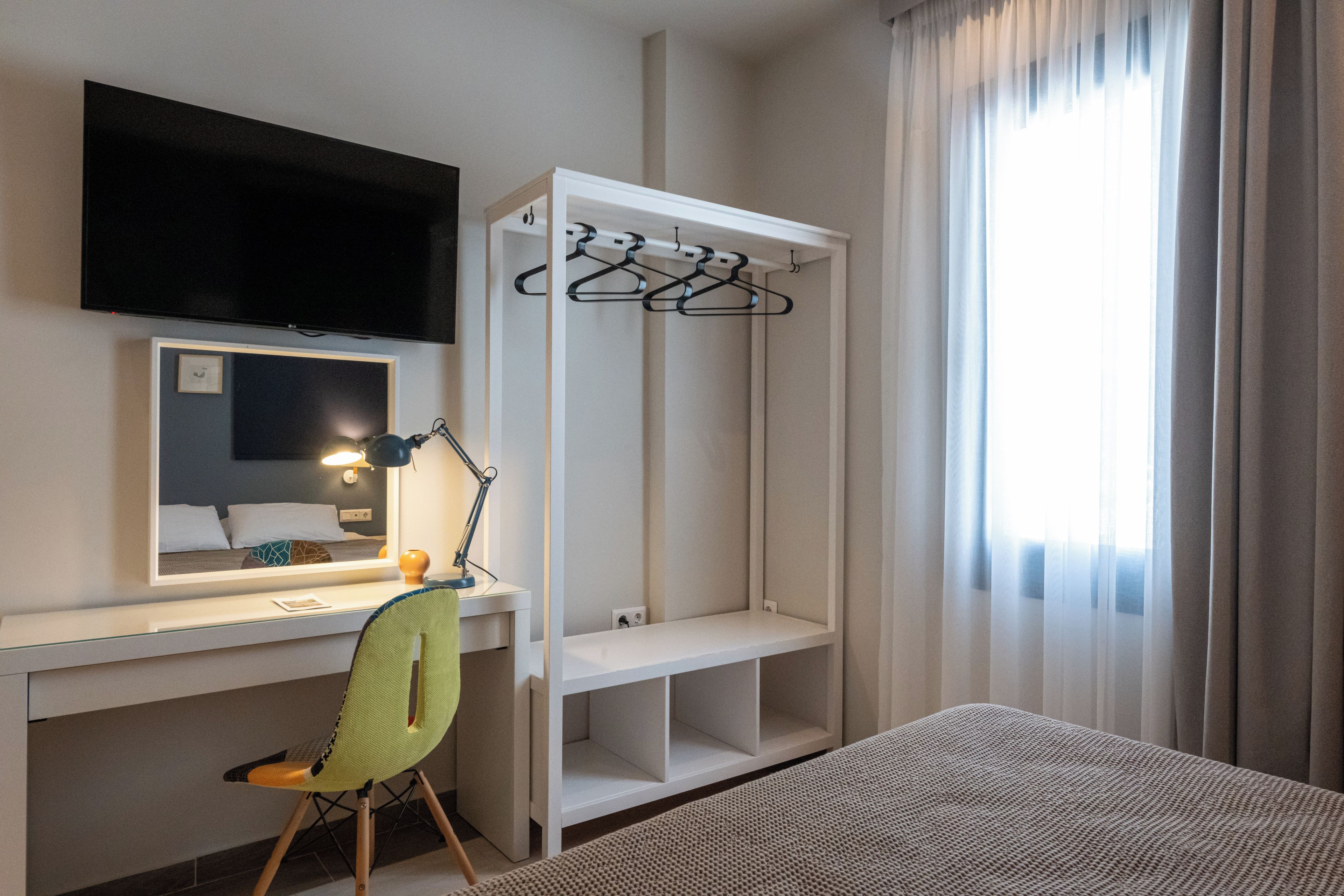 Une chambre d’hôtel équipée d’un bureau, d’une chaise, d’une télévision, d’une armoire et d’une fenêtre avec des rideaux.