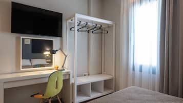 Une chambre d’hôtel équipée d’un bureau, d’une chaise, d’une télévision, d’une armoire et d’une fenêtre avec des rideaux.
