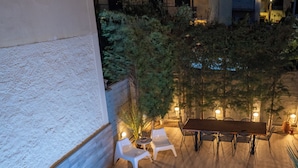 Une piscine extérieure avec une terrasse en bois, entourée de chaises et d’une table, et un bâtiment en arrière-plan.