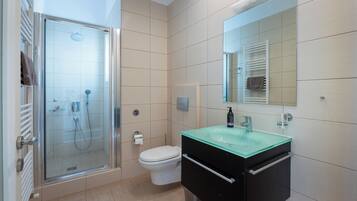 Une salle de bain moderne avec une douche à l’italienne en verre, des toilettes blanches et un meuble-lavabo noir doté d’un vasque en verre.