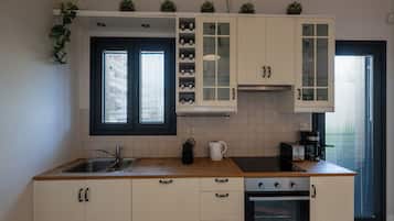 Une cuisine équipée d’un évier, d’une cuisinière, de placards et d’une fenêtre avec des stores.
