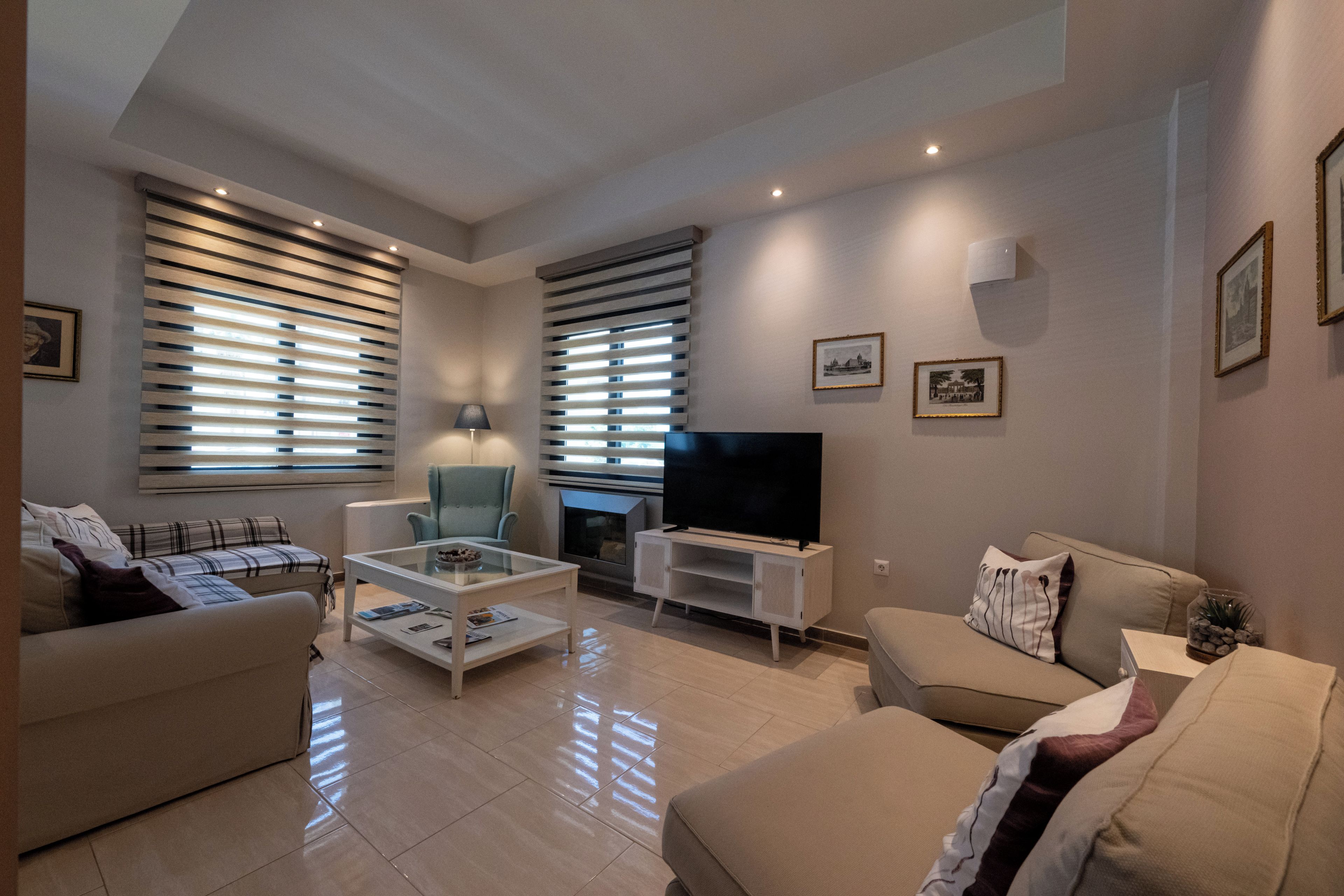 Una sala de estar moderna con sofá, sillón, mesa de centro, televisor, chimenea y ventanas grandes con persianas.