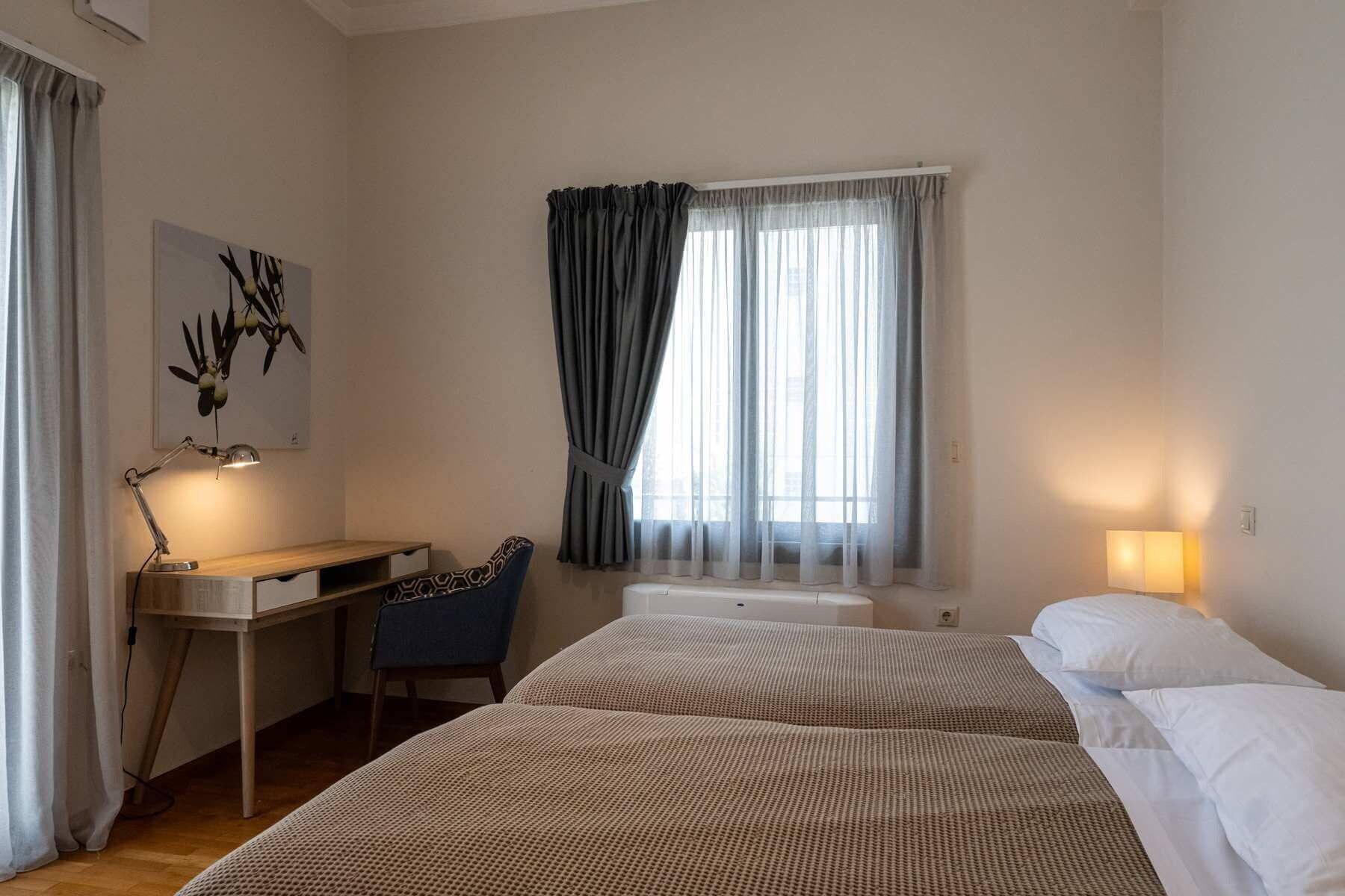Ein Hotelzimmer mit einem Bett, einem Schreibtisch mit Stuhl, einer Lampe und einem Fenster mit Vorhängen.