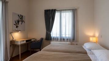 Una camera d'albergo con un letto, una scrivania con una sedia, una lampada e una finestra con tende.