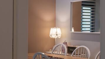 Ein Essbereich mit Holztisch, weißen Stühlen, Pendelleuchten, einer Tischlampe und einem Fenster mit Jalousien.