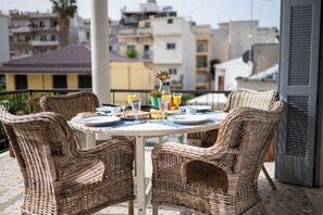 Une table ronde entourée de chaises en osier, sur un balcon donnant sur une vue panoramique de la ville.