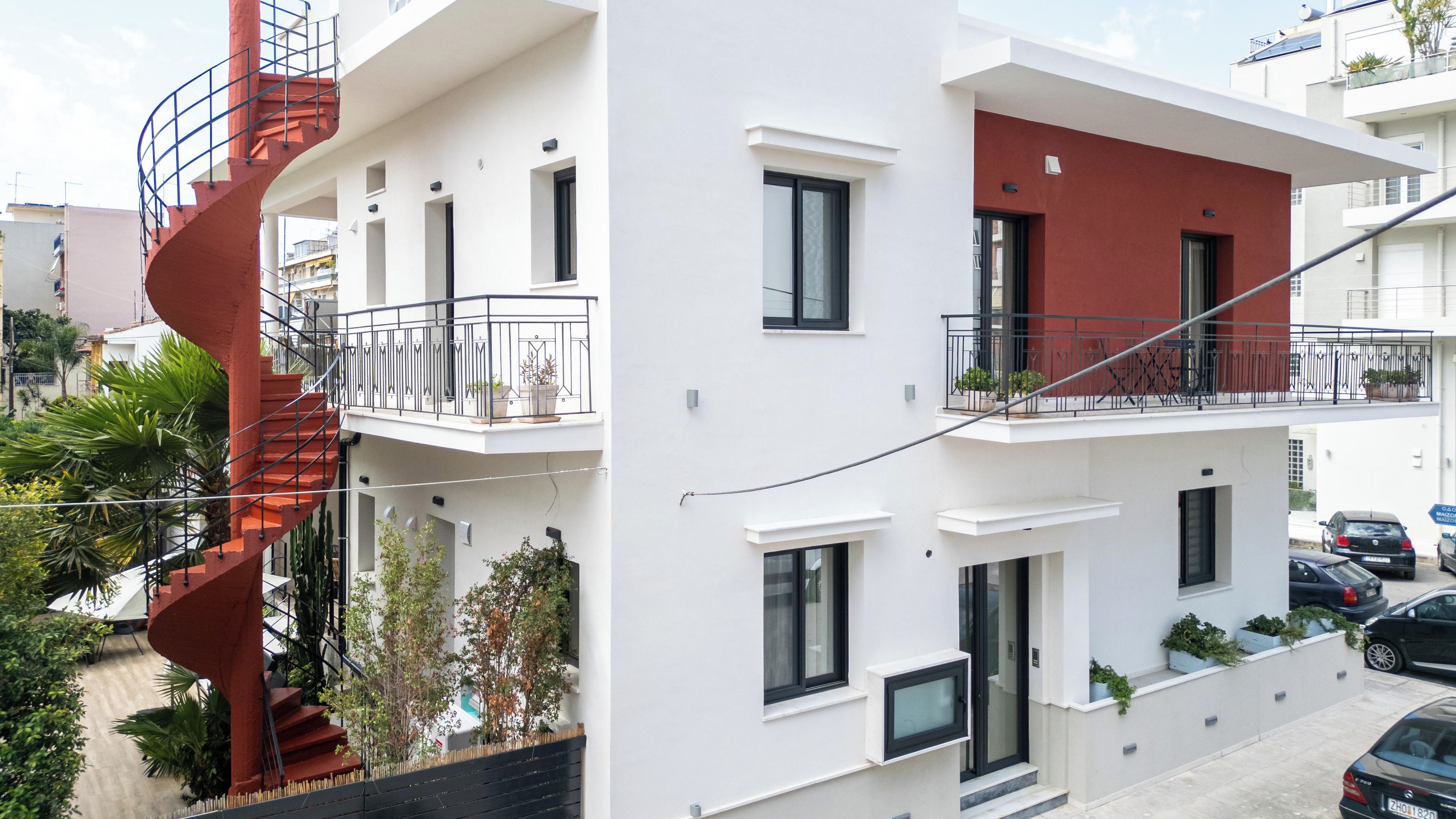 Un edificio moderno de dos pisos con balcones, una escalera espiral y plantas en macetas.
