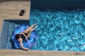 Une personne allongée sur un tube gonflable bleu dans une piscine dont l’eau est d’un bleu limpide.