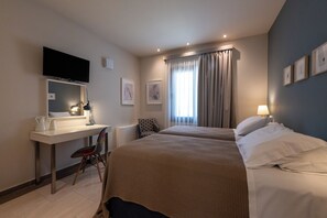 Une chambre d’hôtel avec deux lits, un bureau doté d’un téléviseur à écran plat, une chaise et une fenêtre avec des rideaux.