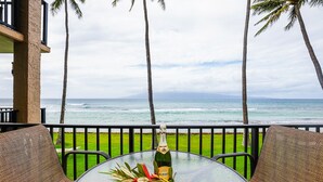 Ein Glastisch mit einer Champagnerflasche und tropischen Blättern auf einem Balkon mit Meerblick.