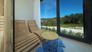Un balcon avec un banc en bois et une petite table ronde, donnant sur un espace aménagé avec des arbres et des rochers.