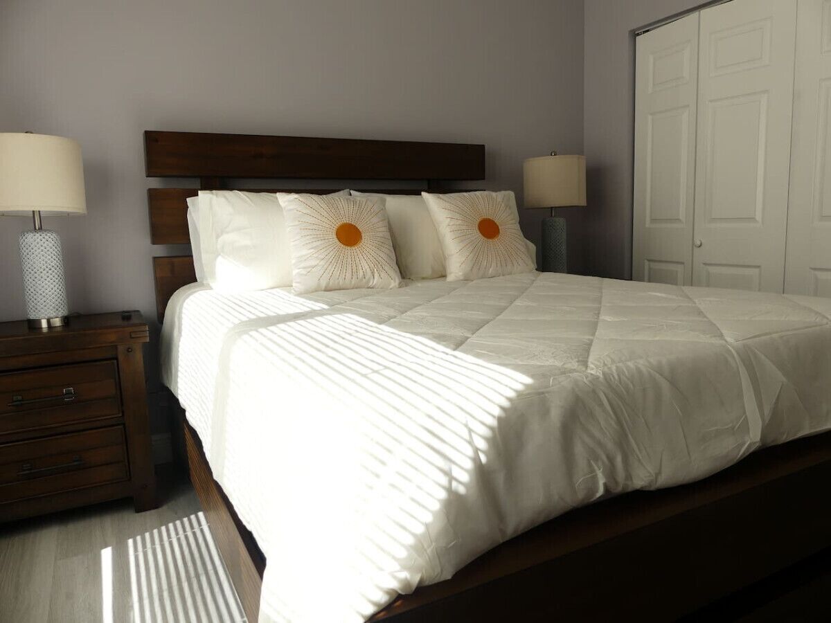 Een keurig opgemaakt bed met een houten hoofdbord, twee bedlampen en een witte kledingkast in een slaapkamer.