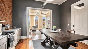 A modern kitchen with a large wooden table, a brick wall, and a view into a dining area. - Executive Suite (Marshall)