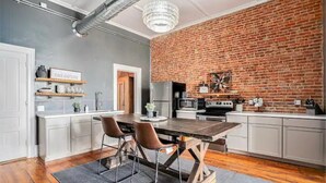 A modern kitchen with a brick wall, white cabinetry, and a wooden dining table with chairs. - Executive Suite (Marshall)