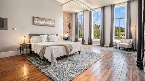 A bedroom with a large bed, a brick accent wall, and a view of the outdoors through large windows. - Executive Suite (Marshall)