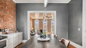 A spacious dining area with a long wooden table, a brick wall, and a view of a building through arched windows. - Executive Suite (Marshall)