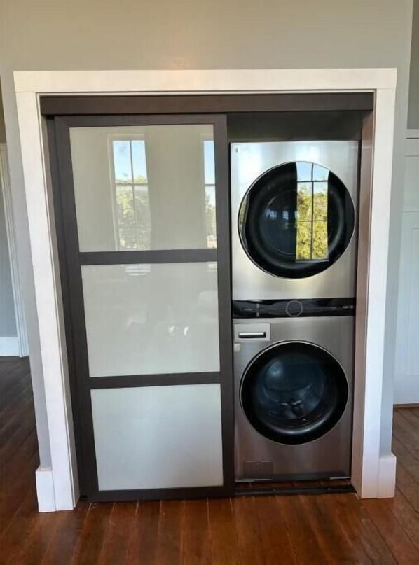 A compact laundry room with two stacked front-loading washing machines and a glass door. - Executive Suite (Marshall)