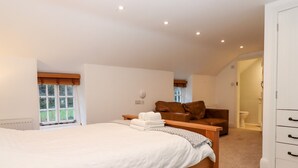 A bedroom with a large bed, a wooden bench, a brown leather sofa, and a white wardrobe. - Trentishoe Coombe (Barnstaple)