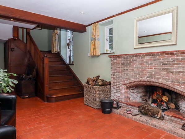 A staircase leading to a second floor, a brick fireplace with logs, and a wicker basket with firewood.