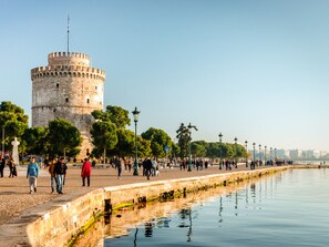 A historic tower with a circular base and a flat top, surrounded by a waterfront promenade with trees and lampposts. - Sanders Tower Centre - Lively Superior Studio Apt (Thessaloniki)