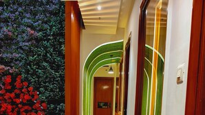 Un passadís amb barana de vidre, un arc il·luminat de verd i una porta amb el número 004.