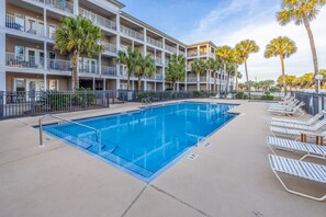 Une piscine avec des chaises longues, des palmiers et un immeuble à plusieurs étages doté de balcons.