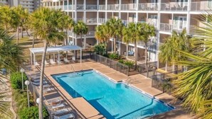 Ein Hotel mit Swimmingpool, umgeben von Palmen und einem mehrstöckigen Gebäude mit Balkonen.