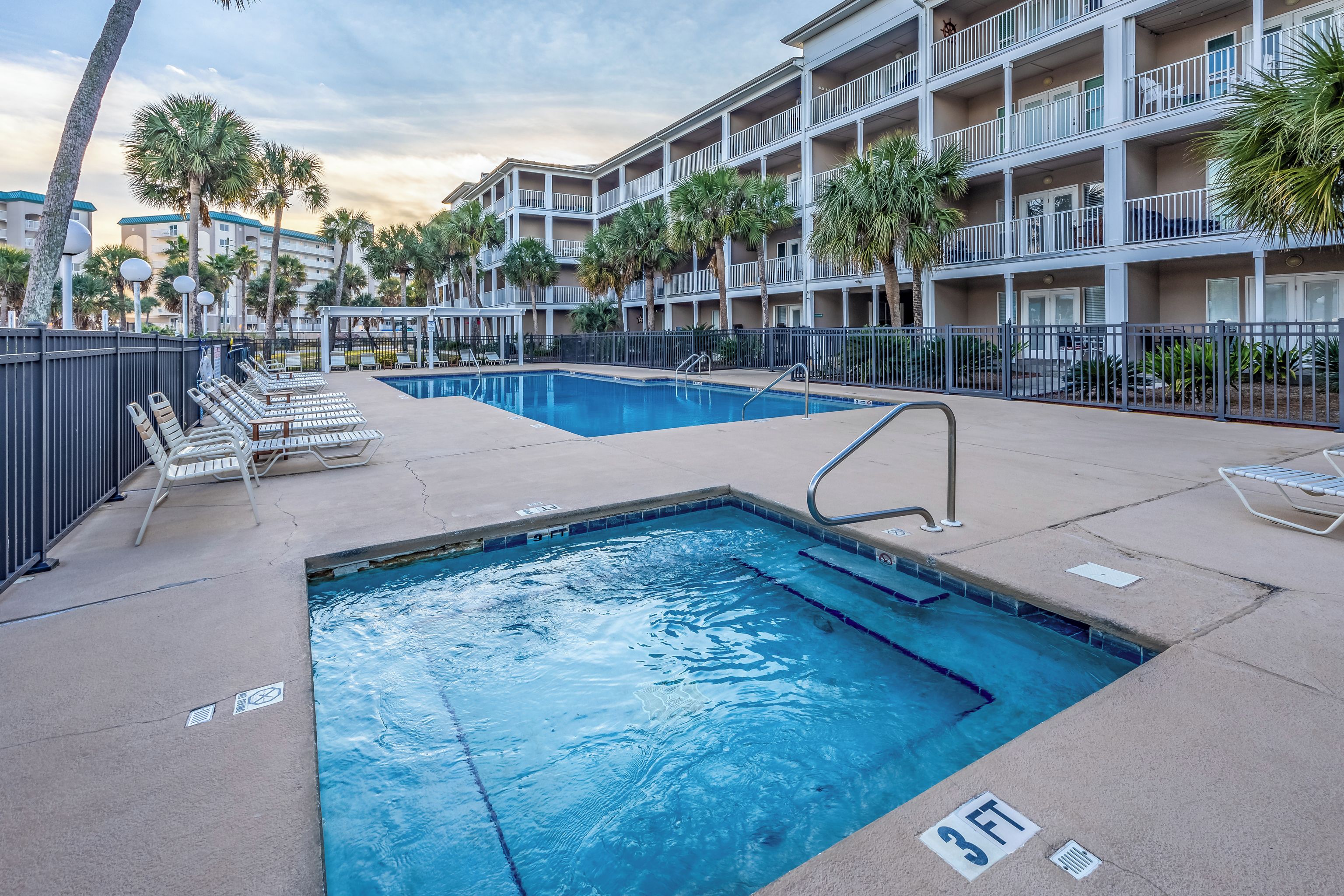 A swimming pool area with lounge chairs and a multi-story building in the background.