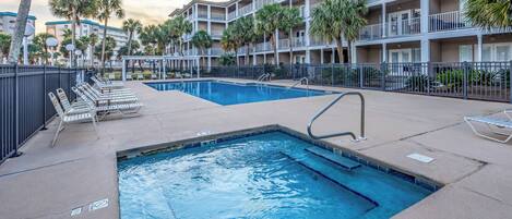 A swimming pool area with lounge chairs and a multi-story building in the background.