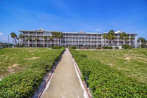 A multi-story hotel with a central pathway flanked by well-maintained lawns and palm trees.