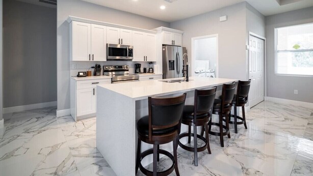 A modern kitchen with white cabinets, stainless steel appliances, and a marble floor.