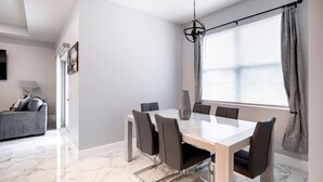A modern dining area with a marble floor, a glass-top table, and black chairs.