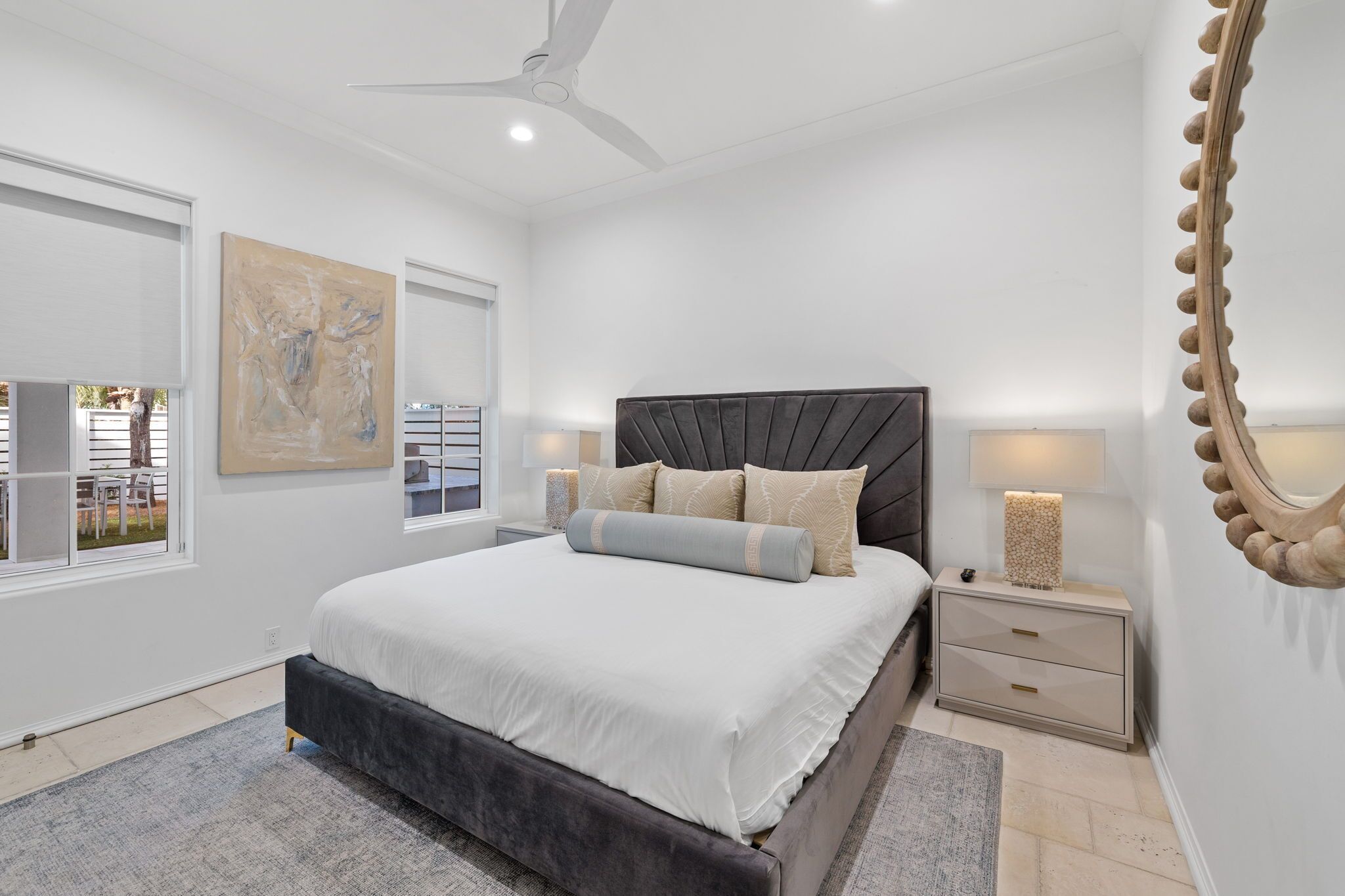 A modern bedroom with a large bed, a ceiling fan, and a view of the outside.