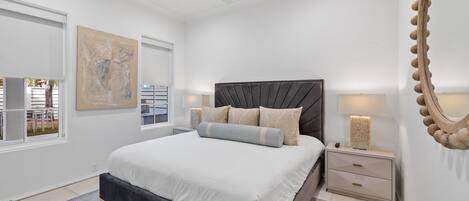 A modern bedroom with a large bed, a ceiling fan, and a view of the outside.