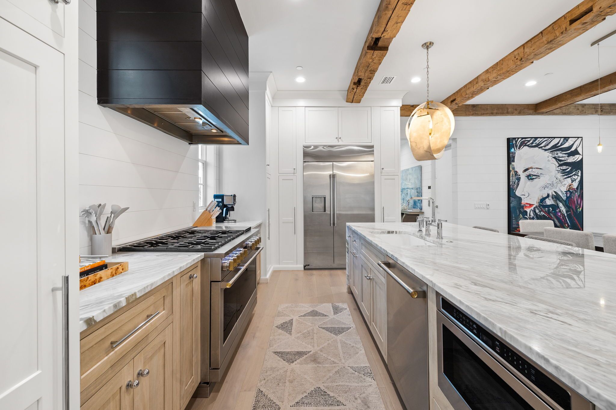 A modern kitchen with white cabinetry, a stainless steel refrigerator, a built-in oven, and a marble countertop.