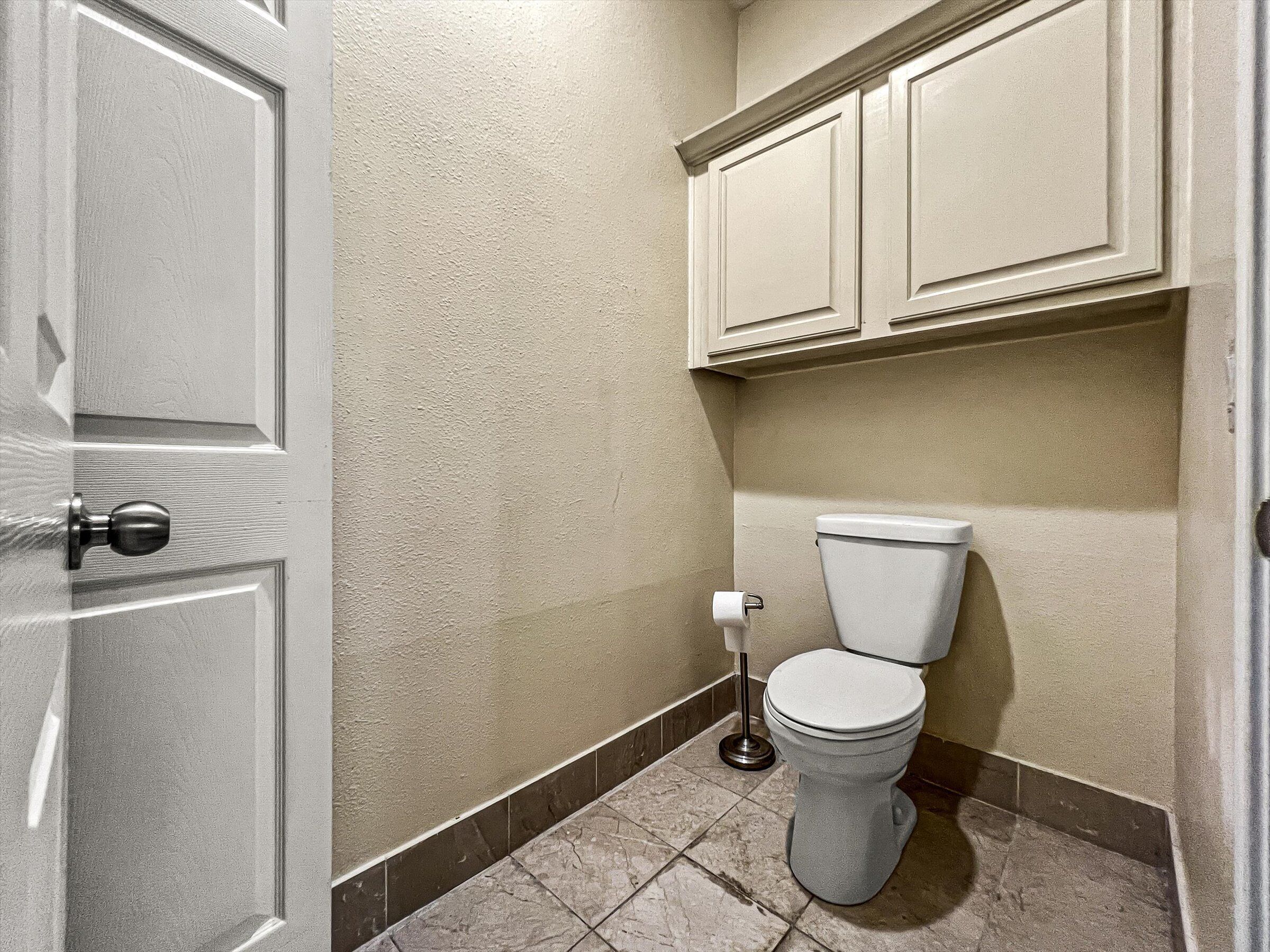 Casa de banho com sanita, suporte para papel higiénico e porta com puxador redondo.