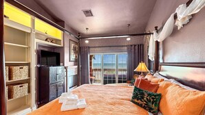A hotel room with a large bed, a television, a balcony with a view, and a wardrobe with shelves. - Elegant Beach Condo, Amazing Ocean Views, W/D (Galveston)