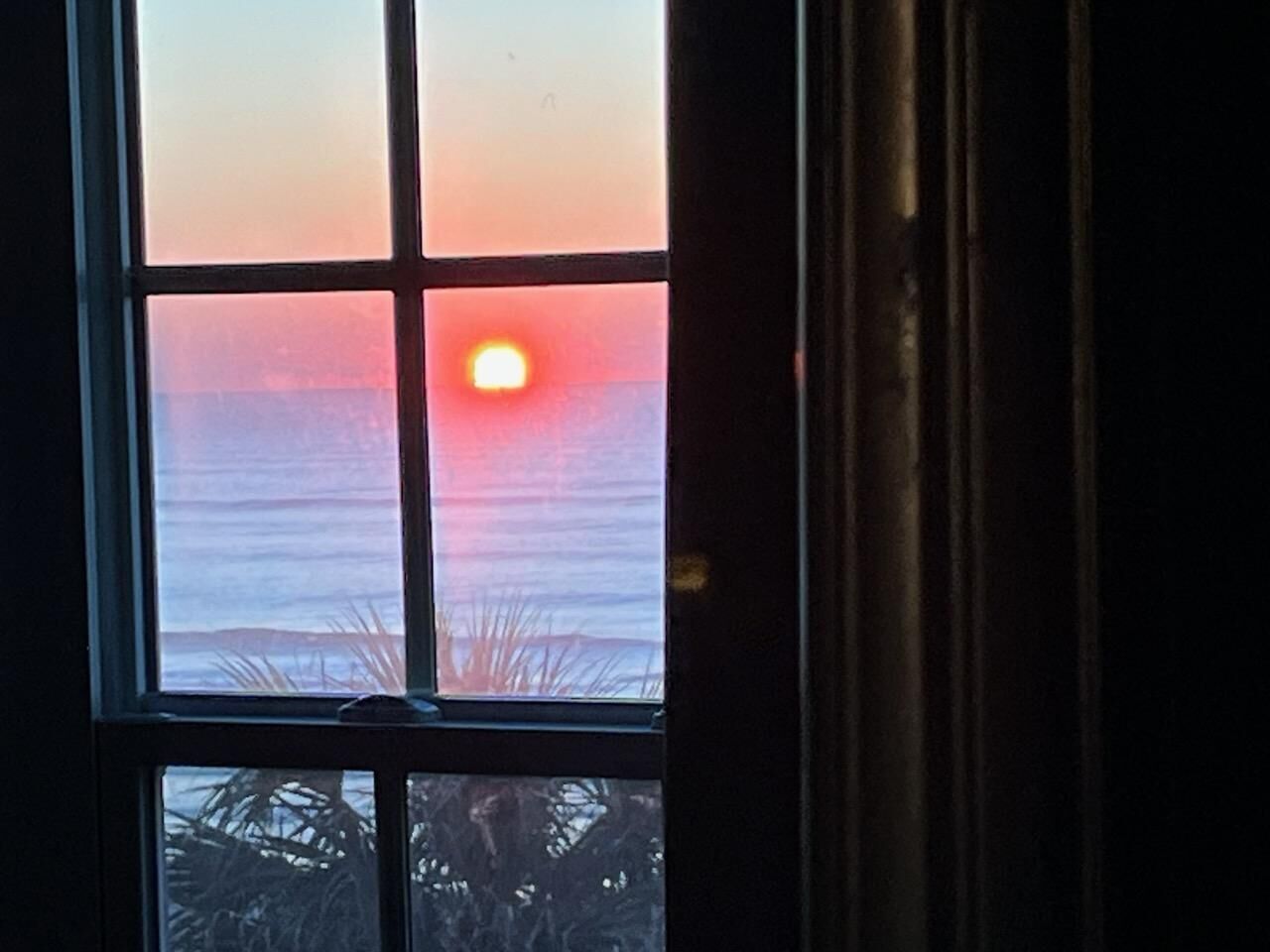 Een raam met uitzicht op de ondergaande zon boven de oceaan.