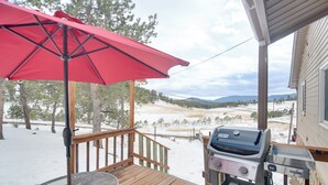 Eine Holzterrasse mit einem roten Sonnenschirm, einem Grill und Blick auf eine verschneite Landschaft mit Bäumen und Bergen.