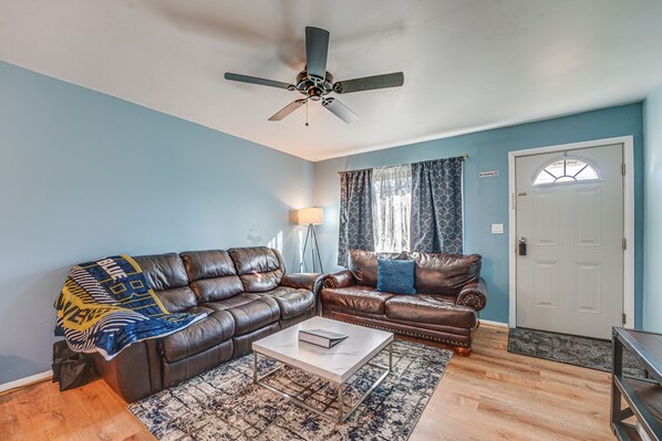 A living room with two leather sofas, a coffee table, a ceiling fan, a patterned rug, and a door with a window.