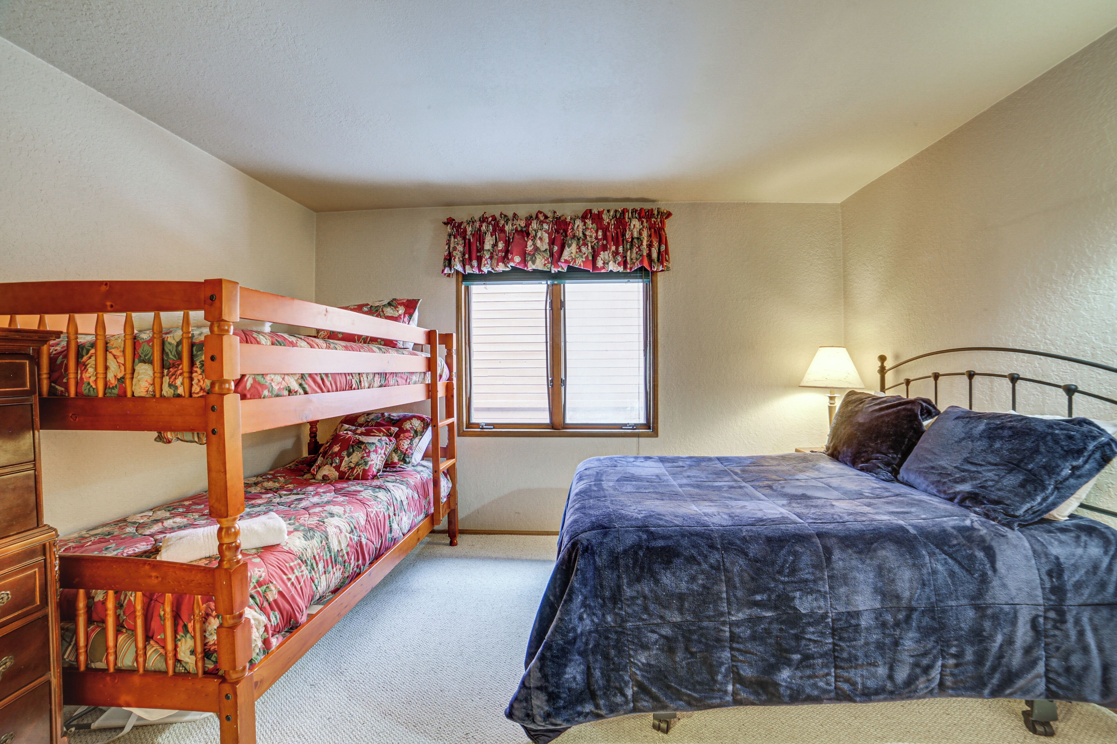 A bedroom with a bunk bed, a single bed, a window with blinds, and a lamp.