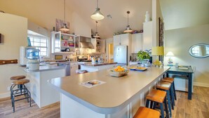 A modern kitchen with a central island, bar stools, pendant lighting, and a view of the dining area.