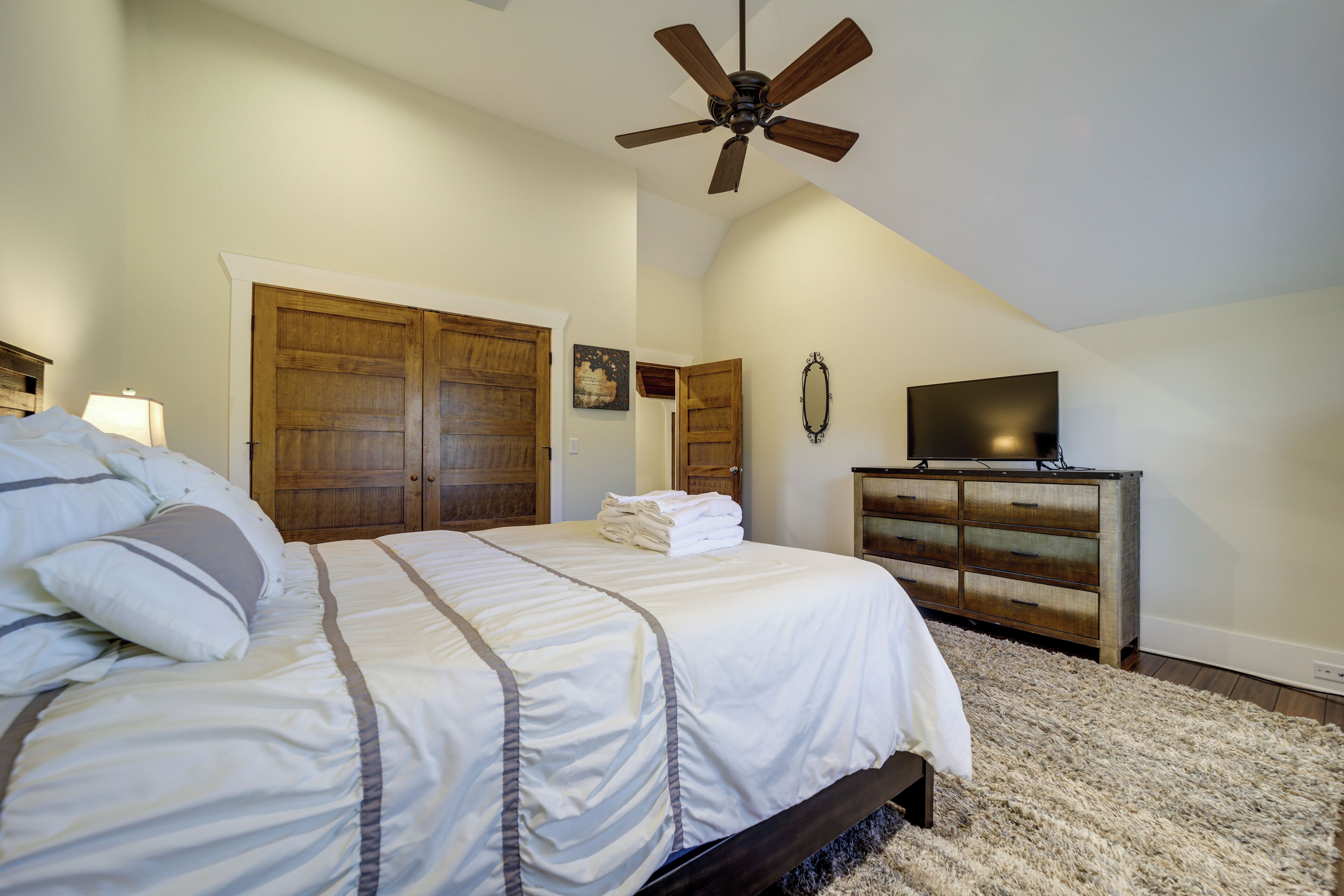 A bedroom with a bed, wooden wardrobe, a television on a dresser, and a ceiling fan.